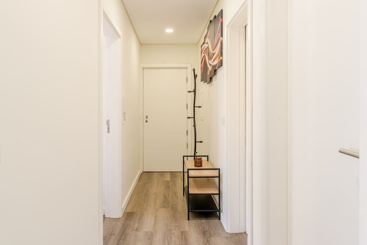 A hallway with a wooden floor, a coat rack, and a door at the end.
