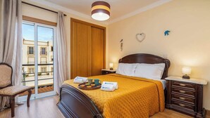 Une chambre d’hôtel comprenant un lit, une table de chevet, une chaise, une fenêtre avec des rideaux et une vue sur les bâtiments environnants.