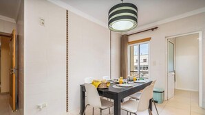 Un espace repas avec une table noire, des chaises blanches et un luminaire suspendu.