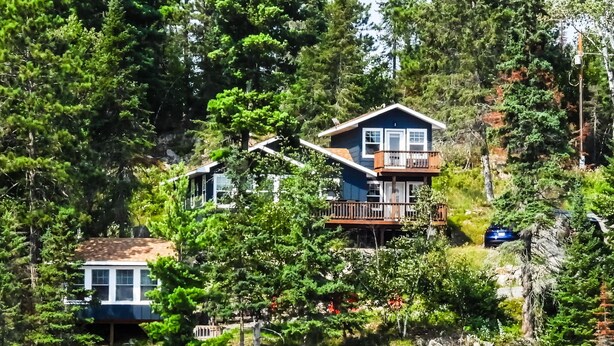 A house with a balcony, surrounded by dense forest and a rocky shoreline. - Comfort and Convenience. Family and pet friendly. Close to the action! (International Falls)