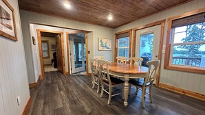 A dining area with a wooden table and chairs, a wooden floor, and a view of a lake through large windows. - Comfort and Convenience. Family and pet friendly. Close to the action! (International Falls)