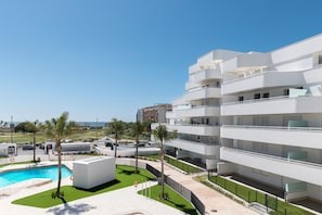 A modern multi-story building with a pool area, palm trees, and a clear sky.