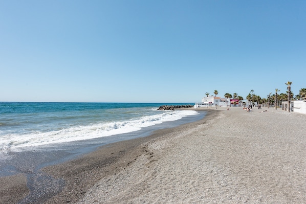 A beach with a building, palm trees, and a clear sky.