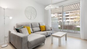 Ein modernes Wohnzimmer mit einem grauen Sofa, einem weißen Couchtisch und einem großen Fenster mit Blick auf einen Balkon.
