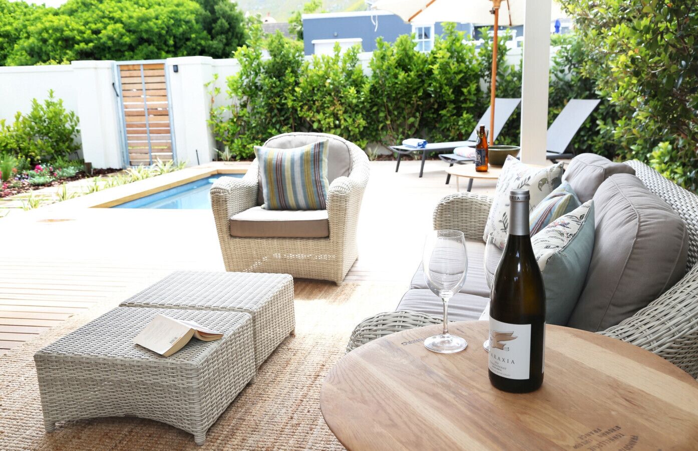 A patio with wicker furniture, a pool, and a bottle of wine.