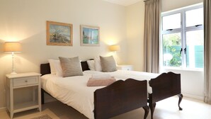 A neatly arranged bedroom with a bed, two bedside tables, lamps, and two framed paintings on the wall.