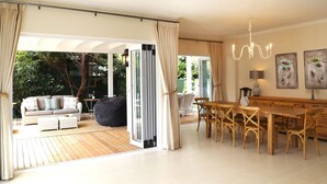 A spacious living area with a wooden deck, a dining table with chairs, and a sofa set.