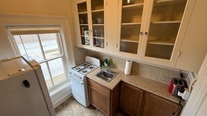 Une cuisine de taille réduite, équipée d’une cuisinière à gaz, d’un évier et de meubles de rangement en bois.