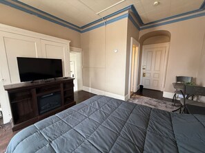 A bedroom with a large bed, a TV on a wooden stand, a door, and a chair.