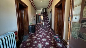 Un couloir avec un tapis à motifs, des portes en bois, un radiateur et un escalier menant à l’étage supérieur.