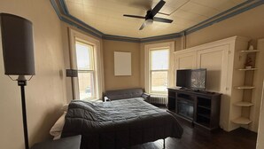 Une chambre à coucher avec un lit, un téléviseur, un ventilateur de plafond et un radiateur.