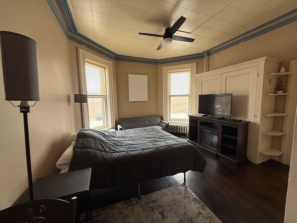 A bedroom with a bed, a TV, a ceiling fan, and a radiator.
