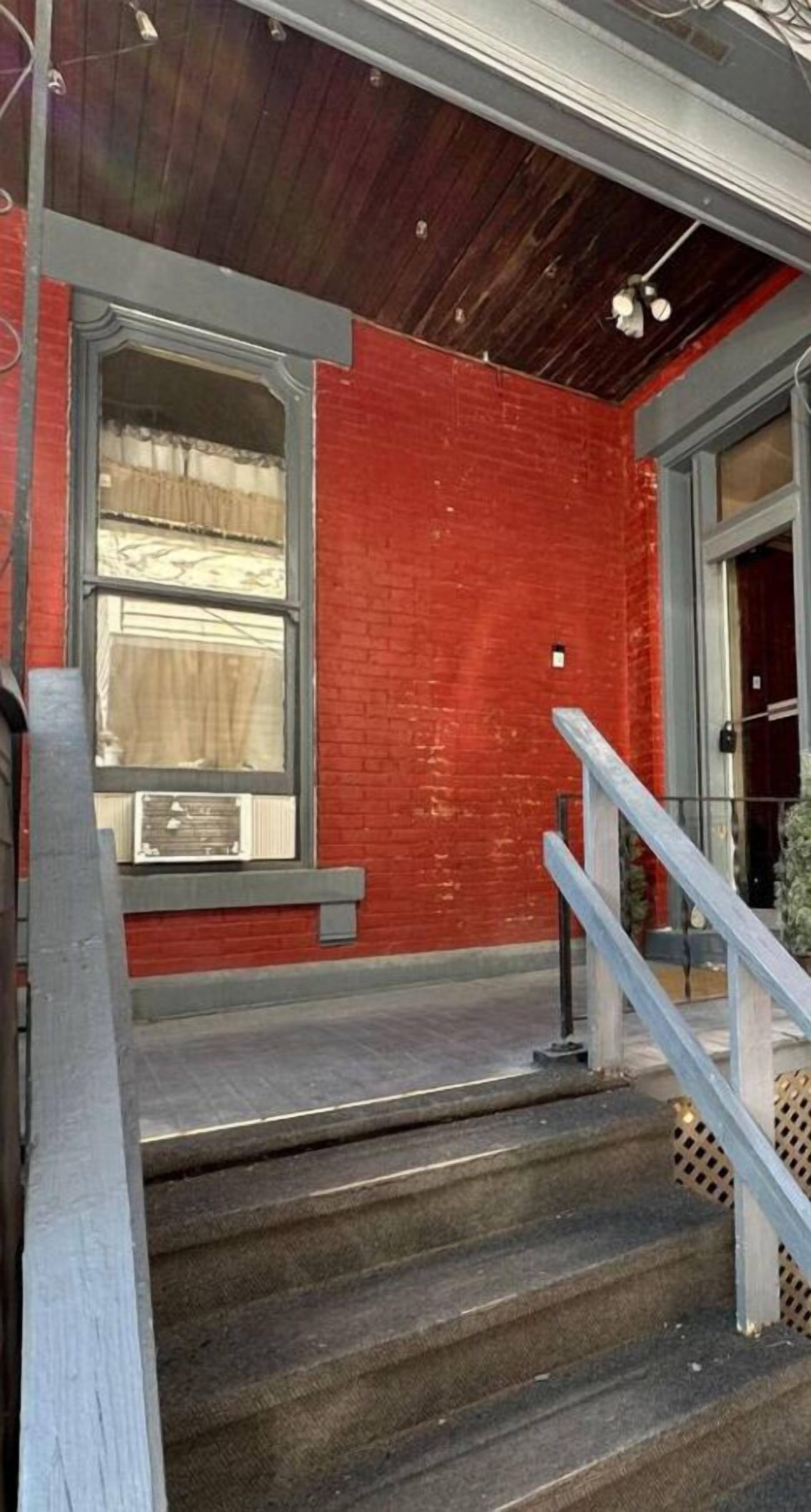 Un escalier menant à une porte, avec un mur en briques rouges et une fenêtre ornée de rideaux.