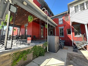A red building with a covered outdoor seating area, a small utility room, and a staircase leading to an upper level.