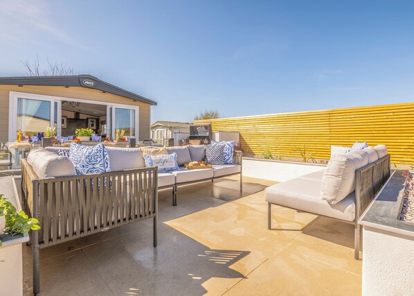 Une terrasse avec des meubles d’extérieur, un barbecue et un mur jaune.