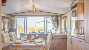 A dining area with a table set for four, a chandelier, and a view through large windows. - Our WOW Lodge sets the standard for luxury accommodation. (Towyn)