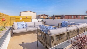 A caravan site with a grey sofa set, a wooden fence, and a clear blue sky. - Our WOW Lodge sets the standard for luxury accommodation. (Towyn)