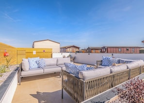 A caravan site with a grey sofa set, a wooden fence, and a clear blue sky.