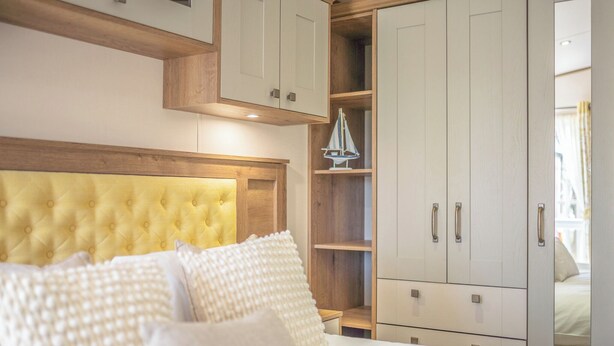 A bedroom with a tufted headboard, a bed with white bedding, a wardrobe with multiple doors, and a small shelf with a decorative item.