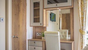 A bedroom with a wooden wardrobe, a bedside table with a mirror, a chair, and a bed.