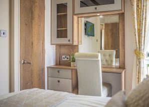 A bedroom with a wooden wardrobe, a bedside table with a mirror, a chair, and a bed.