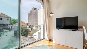 A modern living room with a large window, a flat-screen TV, and a white cabinet.