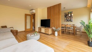 A modern living room with a sofa, a dining table, and a TV. - Deluxe House | Terrace & BBC by HostWise (Parchal)