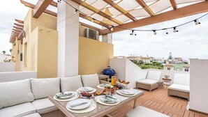 A rooftop terrace with a dining table set for four, surrounded by white sofas and a grill. - Deluxe House | Terrace & BBC by HostWise (Parchal)