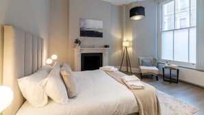 Un dormitorio moderno con una cama grande, una chimenea, una silla y un ventanal.