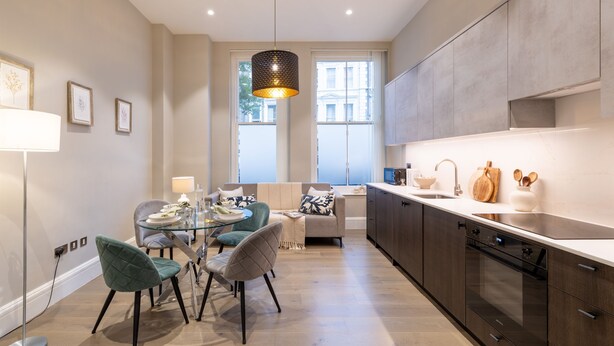 Una cocina moderna con comedor, que incluye una mesa de vidrio, sillas y una lámpara colgante.