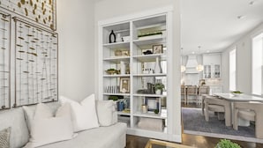 A modern living room with a white sofa, a glass coffee table, and a built-in white shelving unit with decorative items.