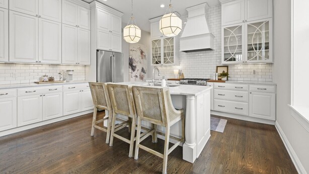 A modern kitchen with white cabinetry, a central island with bar stools, a refrigerator, and a stove.