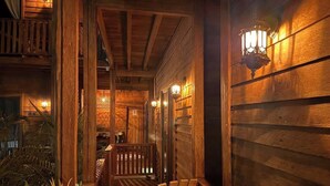 Fachada de madera con una escalera que conduce a un nivel superior, barandilla y luces fijadas a la pared.