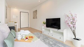 Ein modernes Wohnzimmer mit Flachbildfernseher, einer Essecke mit Tisch für zwei Personen und einer Topfpflanze.