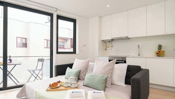 Ein modernes Hotelzimmer mit einem Bett, einer kleinen Küchenzeile und einem Balkon mit Tisch und Stühlen.