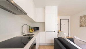 Eine moderne Küche mit schwarzem Arbeitsplatz, Spüle aus Edelstahl und einer Mikrowelle. Im Hintergrund befindet sich ein schwarzes Sofa und eine weiße Tür.