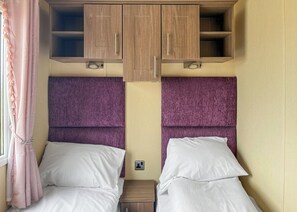Een slaapkamer met twee bedden, een houten garderobe en een raam met gordijnen.