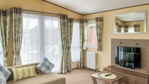 A living room with a sofa, a coffee table, a TV, and curtains. - Platinum 4+2 Hot Tub (Towyn)