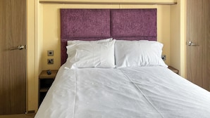 Hotellihuone, jossa on sänky, puinen pääty ja yöpöytä, jossa on kaukosäädin.