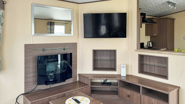 A modern living room with a flat-screen TV, a fireplace, a coffee machine, and built-in wooden cabinets. - Platinum 4+2 Hot Tub (Towyn)