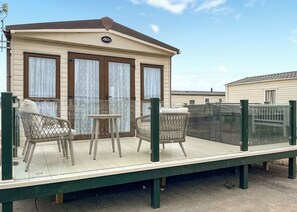 Een caravan met een balkon, twee rieten stoelen en een tafeltje.