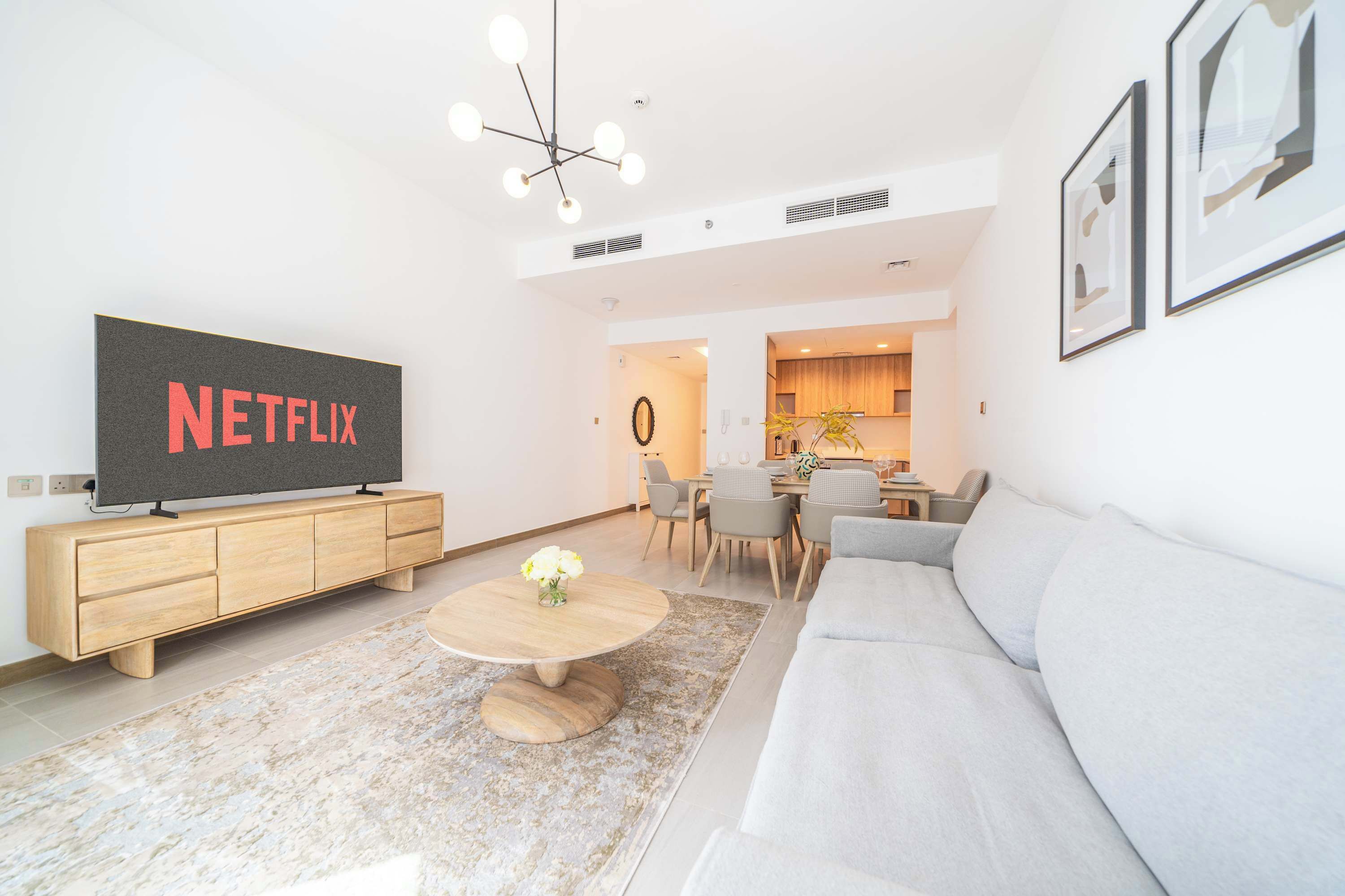 Ein modernes Wohnzimmer mit Flachbildfernseher, Holzschrank, rundem Couchtisch und grauem Sofa.