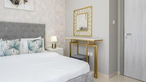 A bedroom with a large bed, a bedside table with a lamp, a gold-framed mirror, and a grey upholstered headboard. - Spacious & Fully Furnished 1BR in Zada (Dubai)
