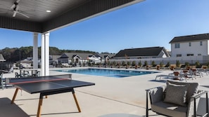 Zona de piscina con sillones, una mesa de ping pong y un área de estar cubierta.