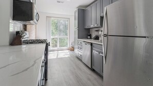 A modern kitchen with stainless steel appliances, a large window, and a view of greenery outside.