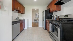 A modern kitchen with wooden cabinets, a black refrigerator, a stove, and a dining area in the background.