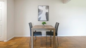 A dining area with a wooden table and four chairs, a small plant on the table, and a large abstract painting on the wall.
