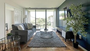 A modern living room with a grey sofa, a glass coffee table, and a large potted plant.