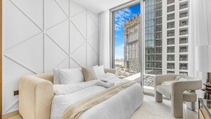 Een moderne slaapkamer met een groot bed, een bank en een stoel, met uitzicht op de stad door grote ramen.