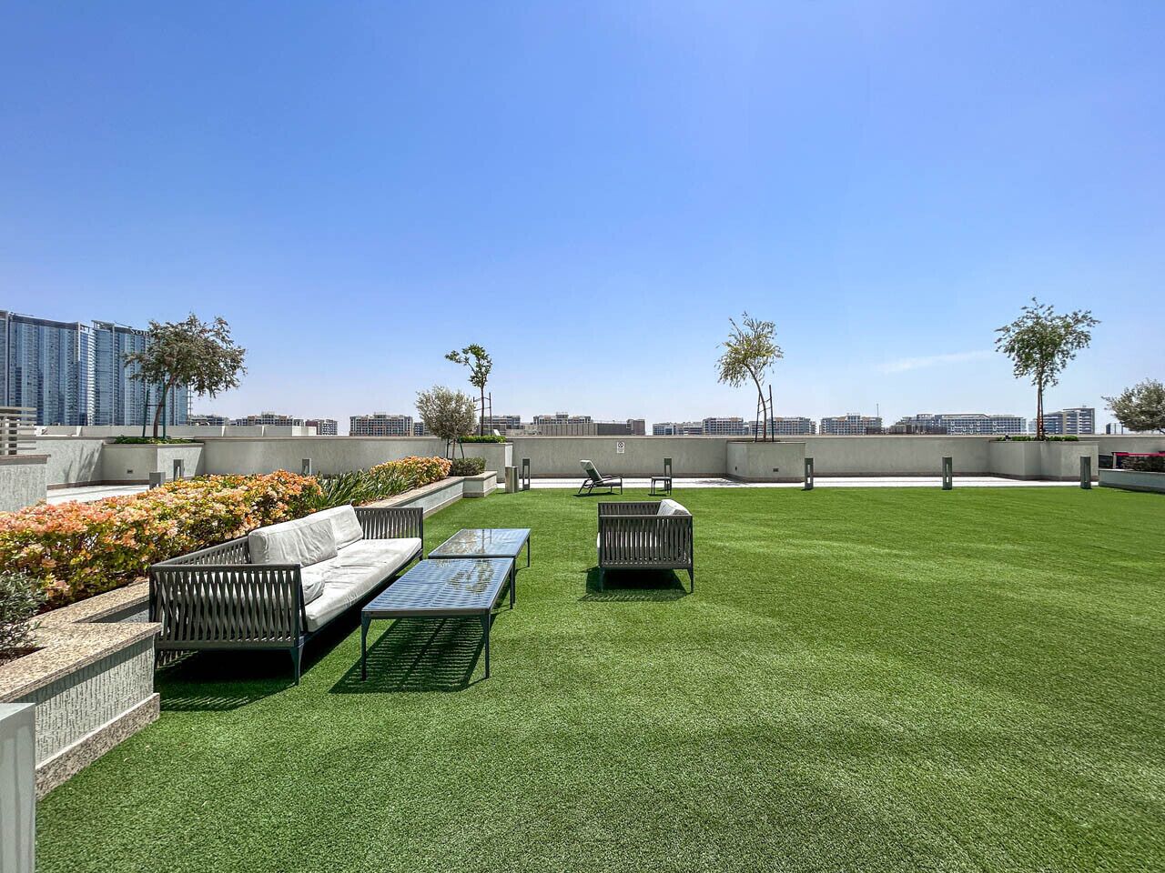 A rooftop garden with artificial grass, two lounge chairs, a sofa, and a small table.